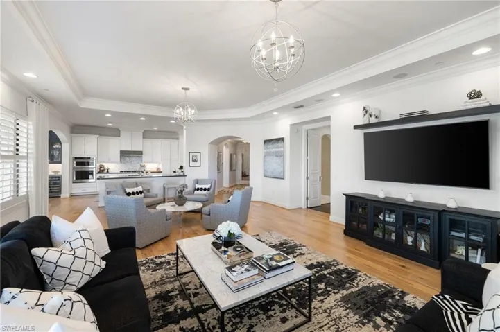 Living room with crown molding, a notable chandelier, a tray ceiling, and light hardwood / wood-style flooring