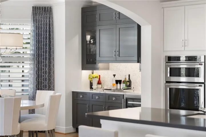 Bar featuring gray cabinets, double oven, beverage cooler, white cabinets, and decorative backsplash