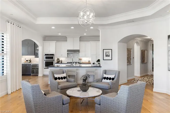 Living room featuring a chandelier, ornamental molding, a raised ceiling, beverage cooler, and light hardwood / wood-style floors