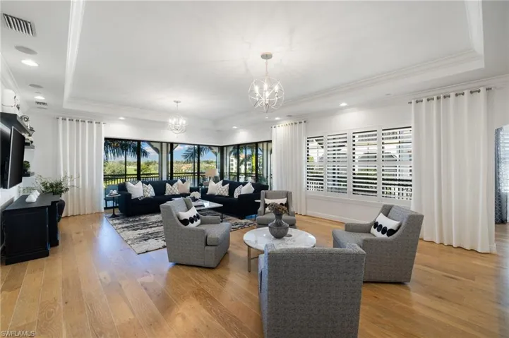 Living room with crown molding, light hardwood / wood-style flooring, an inviting chandelier, and a tray ceiling