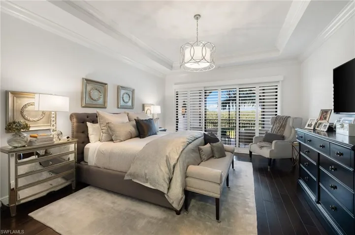 Bedroom featuring dark hardwood / wood-style floors, ornamental molding, access to outside, a raised ceiling, and an inviting chandelier