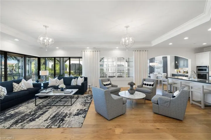 Living room with sink, an inviting chandelier, ornamental molding, a raised ceiling, and light wood-type flooring