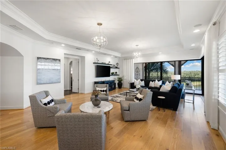Living room with an inviting chandelier, a tray ceiling, light hardwood / wood-style flooring, and ornamental molding
