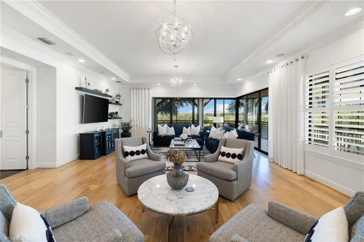 Living room with a raised ceiling, ornamental molding, a notable chandelier, and light hardwood / wood-style flooring
