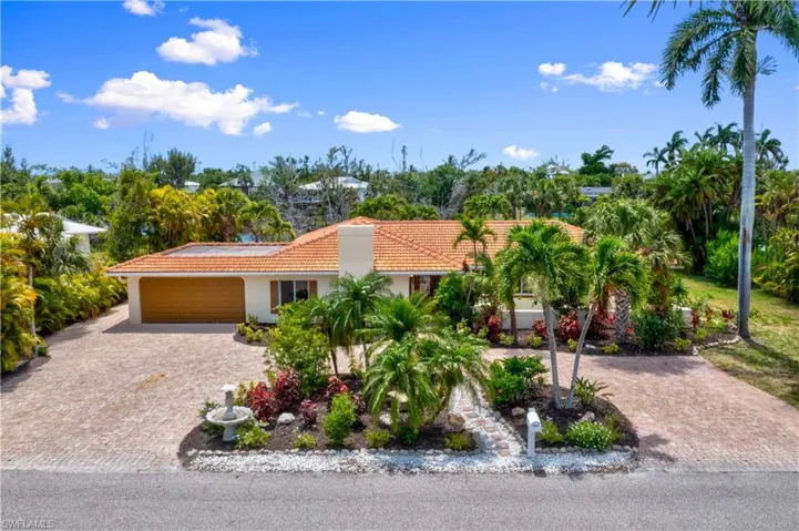 Grand curb appeal with lush tropical landscaping, a circular paved driveway, and a private courtyard entrance.