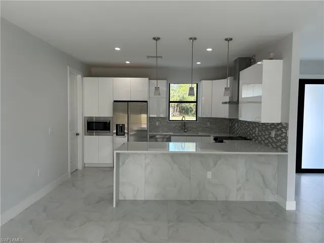 Kitchen with pendant lighting, stainless steel appliances, white cabinetry, and sink