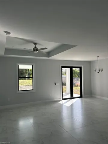 Unfurnished room with plenty of natural light, a raised ceiling, and ceiling fan with notable chandelier