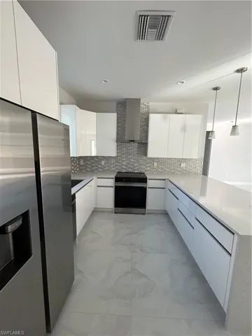 Kitchen featuring white cabinetry, hanging light fixtures, extractor fan, fridge, and electric stove