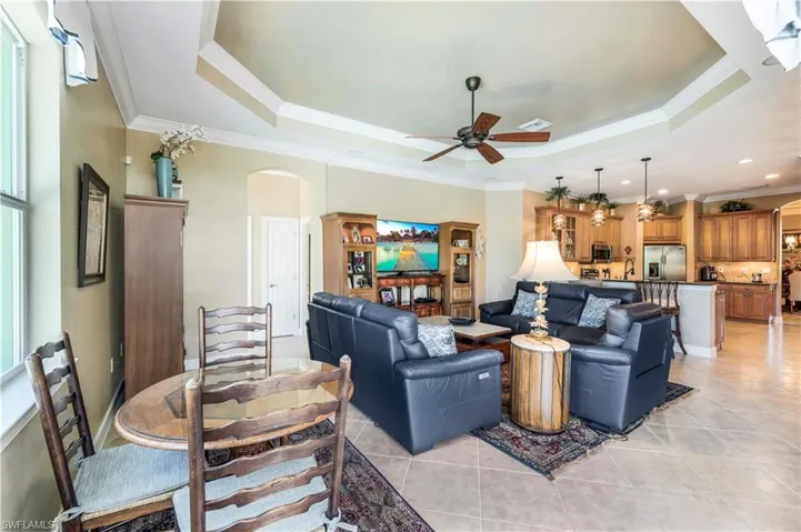 Tiled living room with a healthy amount of sunlight, open concept, tray ceiling, crwon molding and ceiling fan.