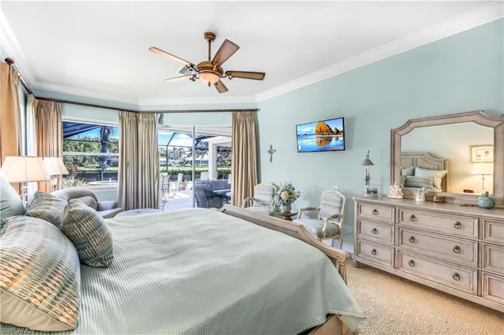 Carpeted master bedroom, access to lanai and pool deck, crown molding and ceiling fan.