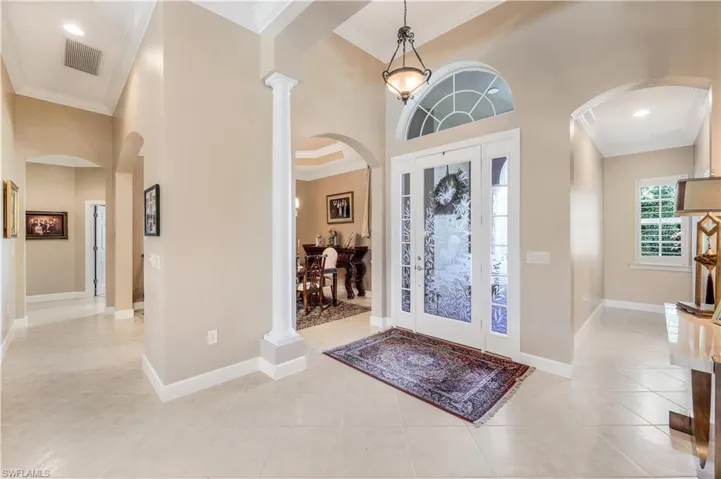 Foyer entrance featuring a custom etched glass front door, ornamental molding, light tile patterned floors, and a towering ceiling