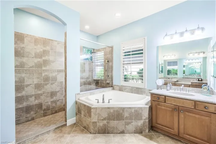 Bathroom featuring tile patterned flooring and wet walls, plus walk in shower, soaking tub, 2 vanities with dressing area.