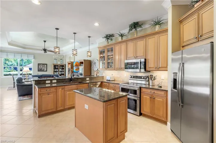 Kitchen featuring kitchen peninsula, dark stone counters, ceiling fan, stainless steel appliances, and a raised ceiling