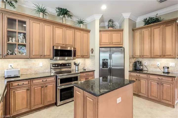 Kitchen with 42' custom wood cabinets, appliances with stainless steel finishes, light tile patterned flooring, granite counters, and a kitchen island.