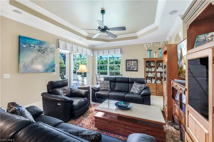 Living room with a raised ceiling, crown molding, and ceiling fan