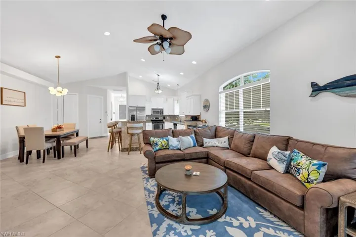 Living room with light tile patterned flooring, ceiling fan with notable chandelier, and vaulted ceiling