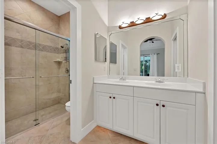 Bathroom featuring toilet, tile patterned floors, an enclosed shower, and double vanity
