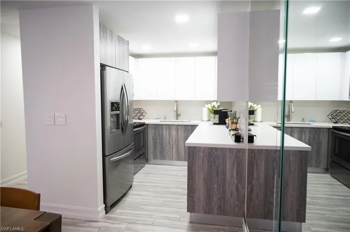 Dual tone kitchen with dual tone cabinetry, modern cabinets, stainless steel appliances, wood finish floors, and light stone countertops