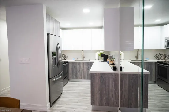 Kitchen featuring two tone color scheme, modern cabinets, stainless steel appliances, wood finish floors, and recessed lighting