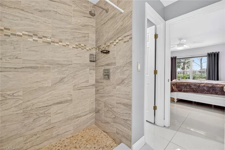 Ensuite bathroom featuring a tile shower, a ceiling fan, and light tile patterned flooring