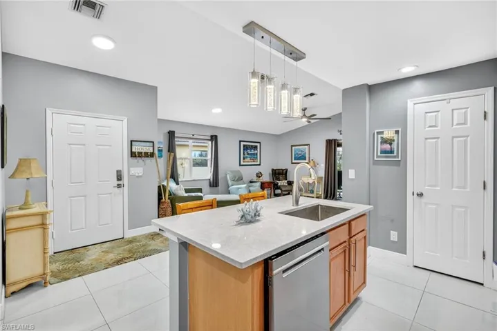 Kitchen with light stone countertops, dishwasher, open floor plan, a kitchen island with sink, and decorative light fixtures