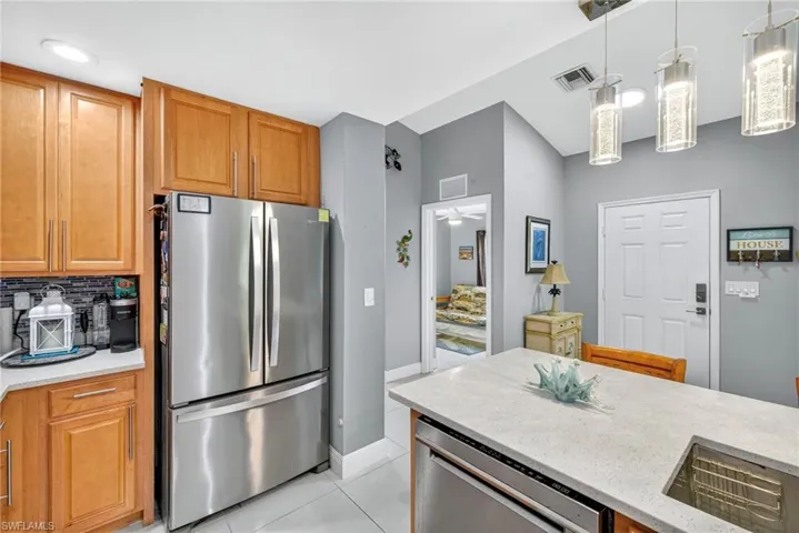 Kitchen featuring stainless steel appliances, light stone countertops, pendant lighting, wood finish cabinetry, and light tile patterned floors