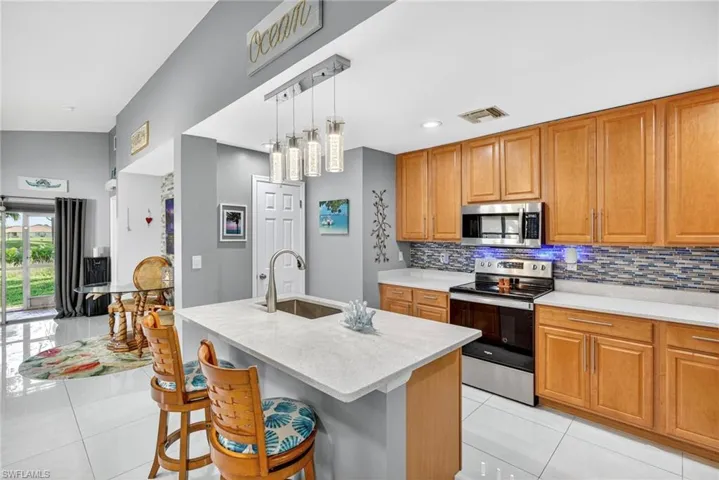 Kitchen featuring stainless steel appliances, light tile patterned floors, wood finish cabinetry, and light stone countertops