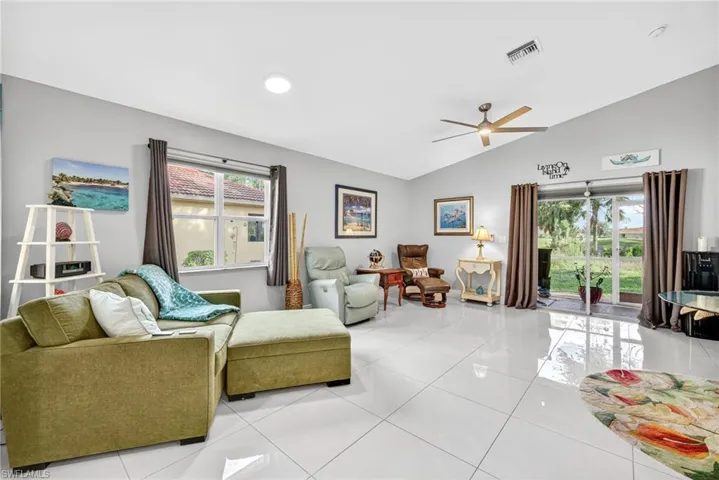Living room with ceiling fan, light tile patterned flooring, and vaulted ceiling