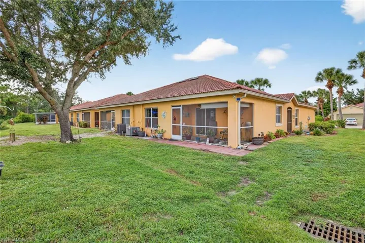 Rear view of house featuring stucco siding, a yard, a sunroom, and a tile roof