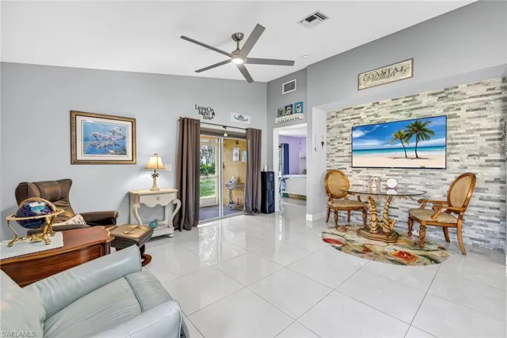 Living room featuring light tile patterned floors, a ceiling fan, an accent wall, and lofted ceiling