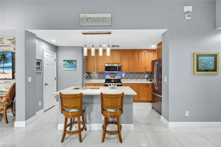 Kitchen with wood finish cabinetry, light tile patterned flooring, stainless steel appliances, and a kitchen bar