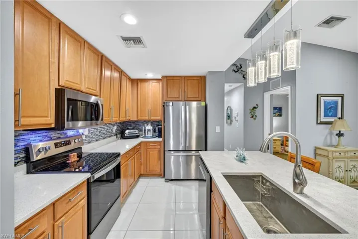 Kitchen featuring stainless steel appliances, pendant lighting, light stone countertops, light tile patterned flooring, and wood finish cabinets