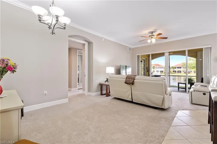 Tiled living room featuring crown molding and ceiling fan with notable chandelier