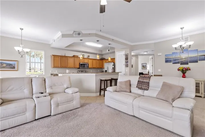 Living room with light carpet, ceiling fan with notable chandelier, and crown molding