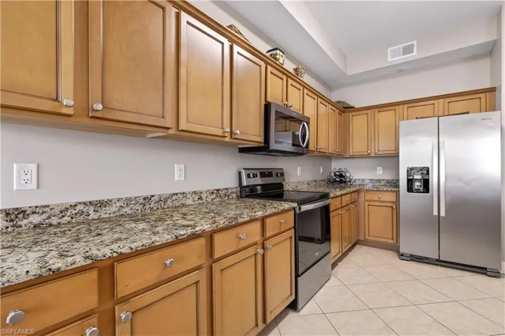 Kitchen featuring light stone counters, appliances with stainless steel finishes, and light tile flooring
