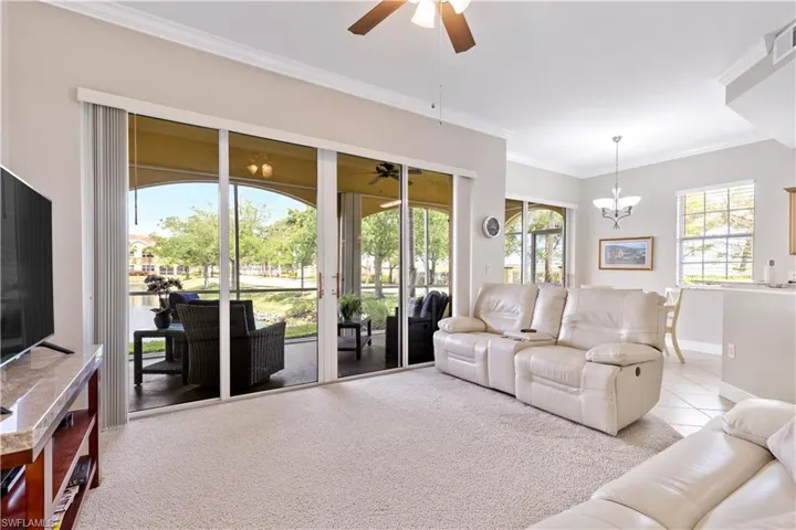 Carpeted living room featuring ornamental molding and ceiling fan with notable chandelier