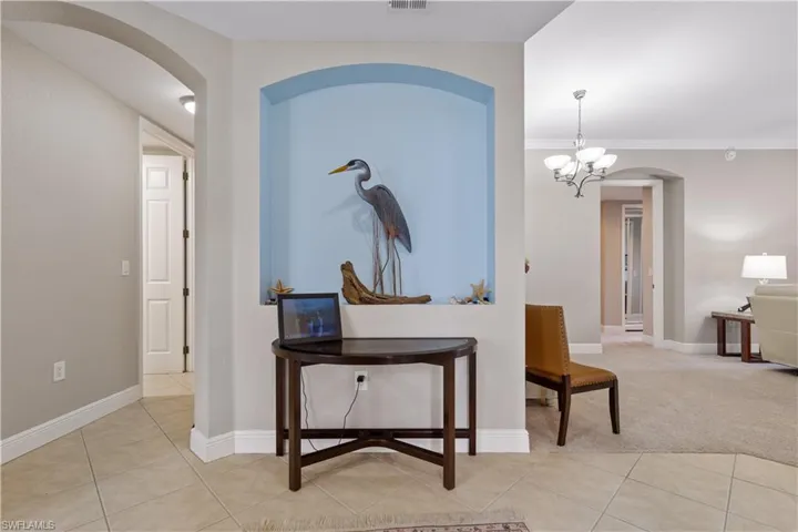 Hallway with an inviting chandelier, ornamental molding, and light tile floors