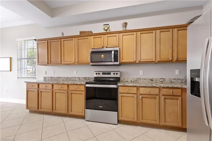 Kitchen with appliances with stainless steel finishes, light stone countertops, ornamental molding, and light tile flooring
