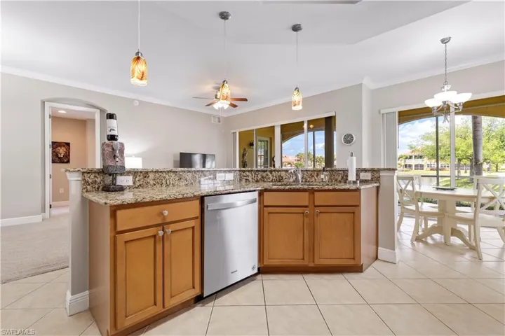 Kitchen with hanging light fixtures, light tile flooring, dishwasher, and ceiling fan with notable chandelier