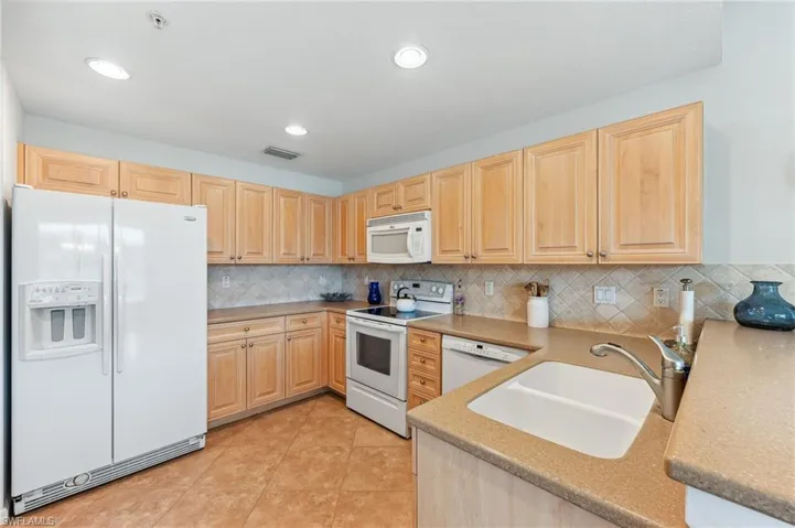 Kitchen featuring white appliances, light brown cabinetry, tasteful backsplash, light tile patterned flooring, and recessed lighting