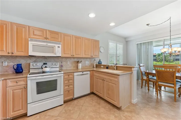 Kitchen featuring white appliances, light brown cabinets, a peninsula, a chandelier, and recessed lighting