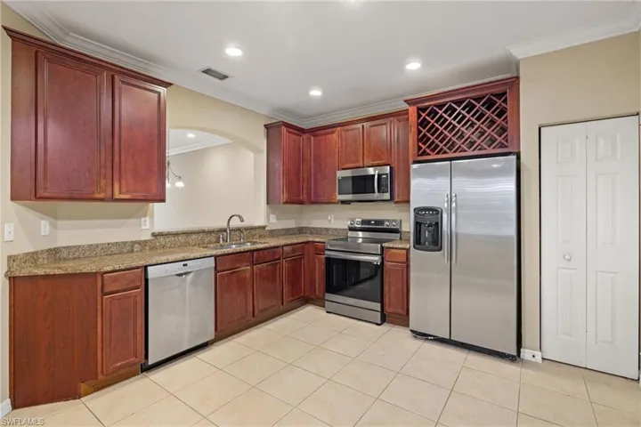Kitchen featuring stainless steel appliances, sink, light stone countertops, light tile patterned floors, and crown molding