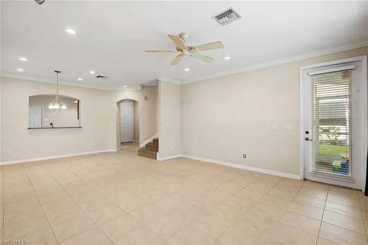 Unfurnished living room with ceiling fan with notable chandelier, light tile patterned floors, and crown molding