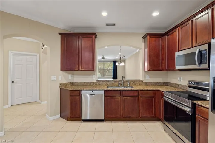 Kitchen with stainless steel appliances, sink, light stone counters, light tile patterned floors, and crown molding