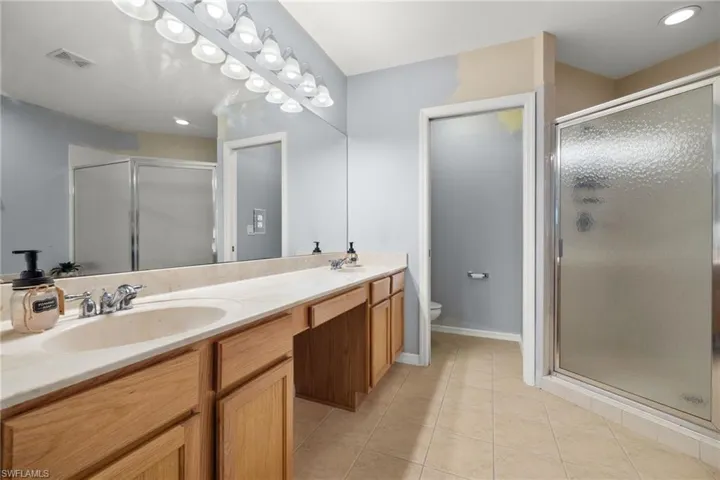 Bathroom with a shower with door, vanity, toilet, and tile patterned floors