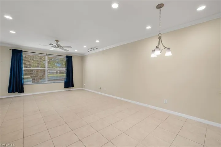 Empty room featuring ceiling fan with notable chandelier, light tile patterned floors, and ornamental molding