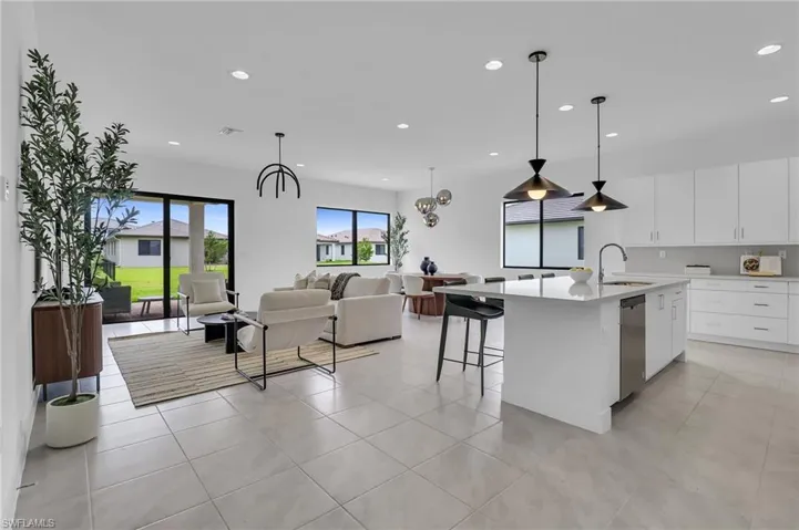 Kitchen featuring recessed lighting, open floor plan, light countertops, stainless steel dishwasher, and a center island with sink
