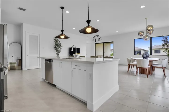 Kitchen with appliances with stainless steel finishes, white cabinets, an island with sink, hanging light fixtures, and recessed lighting