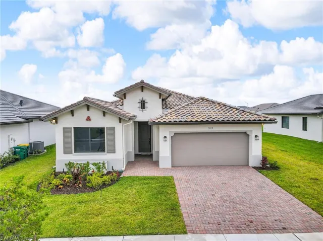 Mediterranean / spanish home featuring stucco siding, decorative driveway, a garage, a front lawn, and a tile roof