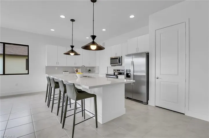 Kitchen featuring appliances with stainless steel finishes, an island with sink, white cabinets, recessed lighting, and a kitchen bar